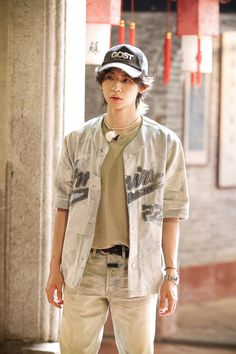 a young man standing in front of a pillar wearing a baseball cap and shirt with writing on it