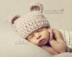 a baby wearing a crocheted bear hat laying on top of a bed with its hands under his chin