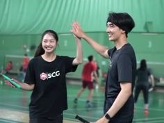 two people standing in a gym holding tennis racquets and giving each other high five