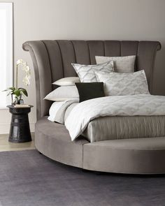 a round bed with pillows and blankets on top of it next to a vase filled with flowers