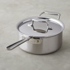 a stainless steel pot with lid and spoon on a white surface, ready to be used for cooking