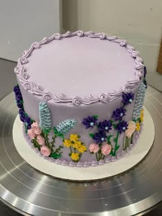 a purple cake with flowers on it sitting on top of a silver platter in front of a white wall