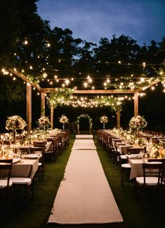 an outdoor wedding venue set up with white linens and greenery, lit by fairy lights