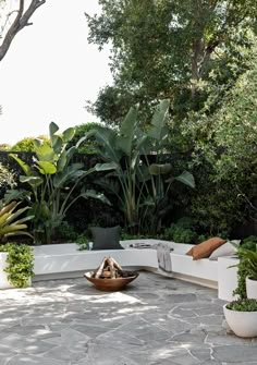 a stone patio with potted plants and seating area in the middle, surrounded by greenery