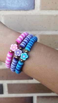 a woman's arm with colorful bracelets and flowers on it, against a brick wall