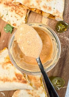 some quesadillas on a cutting board with a spoon and sauce in it