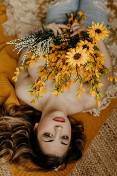 a woman laying on the ground with yellow flowers in her hair and wearing blue jeans