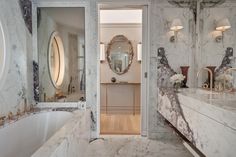 a bathroom with marble walls and flooring next to a bathtub in front of a large mirror