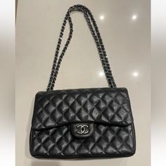 This Chanel Shoulder Bag Is A Timeless Classic, Crafted From Black Quilted Lambskin Leather With Silver Hardware Accents. The Authentic Bag Id# 19277509 The Bag Features A Rectangular Shape With A Turn Lock Closure And Double Handles For Easy Carrying. It Has A Large Size With A Depth Of 3.75 Inches, A Width Of 12 Inches, And A Height Of 8 Inches. The Bag Has Four Inside Pockets And One Outside Pocket, Providing Ample Space For Your Essentials. It Also Comes With A Chain Strap That Can Be Adjust High-end Black Flap Bag For Travel, Double Flap Shoulder Bag With Dust Bag, High-end Travel Shoulder Bag With Cc Turnlock Closure, High-end Black Flap Bag For Business, High-end Black Shoulder Flap Bag, High-end Black Flap Bag, High-end Black Satchel Flap Bag, Black Double Flap Bag For Office, Black Double Flap Shoulder Bag For Office