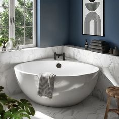 a white bath tub sitting under a window next to a wooden stool and potted plant