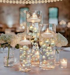 the centerpieces are filled with white flowers and lit candles in glass vases