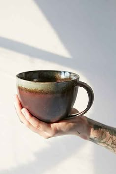 a person holding a coffee cup in their left hand with tattoos on the arm and wrist