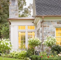 a house that has some flowers in front of it and bushes around the outside area