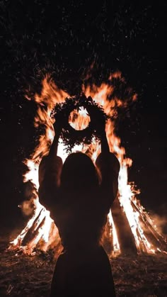 a person standing in front of a fire with their hands up to the sky above them