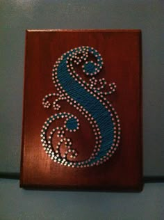 the letter s is made out of beads on a wooden plaque with bead work