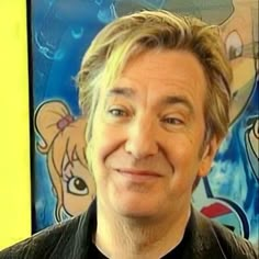 a close up of a person wearing a black shirt and smiling at the camera with cartoon characters behind him