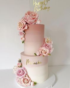 a three tiered cake with pink flowers on the top and happy birthday sign above it