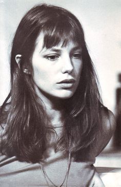 a black and white photo of a woman with long hair looking at the camera while wearing a necklace