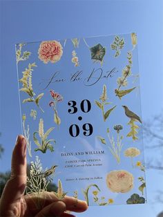 a hand holding up a wedding card with flowers on it and the date in black