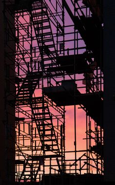 a fire escape is silhouetted against a sunset sky with scaffolding in the foreground