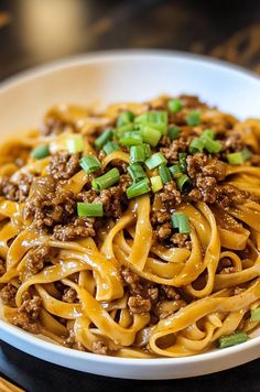 a white bowl filled with noodles and ground beef on top of a wooden cutting board