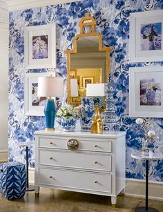 a blue and white room with pictures on the wall, a chest of drawers and a mirror