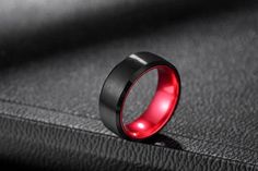 a black and red ring sitting on top of a leather surface with the light shining through it