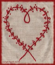 a heart shaped embroidered on top of a piece of cloth with two crossed needles in the middle