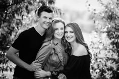 two women and a man are posing for a black and white photo together in front of some trees