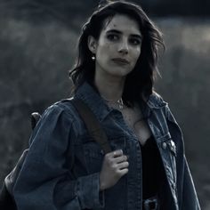 a woman with dark hair wearing a denim jacket and holding a backpack in her hand