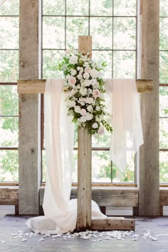 a wooden cross with flowers on it in front of a window at a wedding ceremony