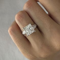 a woman's hand with a diamond ring on top of her finger, showing the center stone