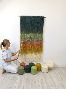 a woman sitting on the floor next to a wall hanging with yarn and crochet