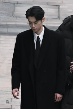 a man in a suit and tie walks down the street with another man wearing a black coat