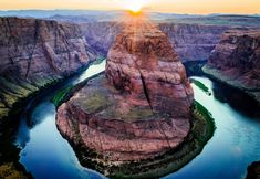 the sun is setting over a canyon with a river running between it and mountains in the background