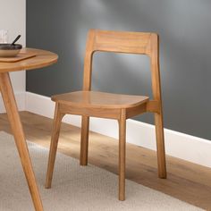 a wooden chair sitting next to a table on top of a carpeted floor in front of a gray wall