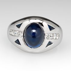 This charming ring is centered with one (1), bezel set, oval cabochon cut natural blue sapphire. The shoulders of the ring are each accented with two (2), flush set, triangle step cut natural blue sapphires and four (4), bead set, old European cut diamond. The ring measures 11.9mm at the top, rises 6.4mm above the finger, tapering to 2.8mm wide and 1.0mm thick at the base of the shank. The ring is currently a size 4.25 and we offer complimentary sizing to fit. Luxury Hallmarked Oval Cabochon Sapphire Ring, Elegant Blue Oval Cabochon Signet Ring, Timeless Cabochon Sapphire Ring, Elegant Sapphire Signet Ring With Gemstone, Formal Polished Finish Oval Cabochon Sapphire Ring, Sapphire Cabochon Diamond Ring, Elegant Sapphire Gemstone Signet Ring, Sapphire Oval Cabochon Ring With Diamonds, Elegant Sapphire Signet Ring