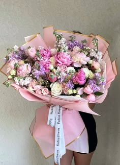 a woman holding a large bouquet of flowers in her hands with a ribbon around it