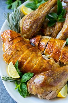 a white plate topped with chicken, lemons and minty garnishes