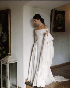 a woman in a white dress standing next to a wall with a painting on it