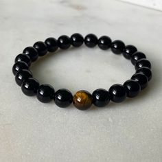 The beauty and wonder of the tiger eye bead culminate with a black onyx beaded bracelet. This is the perfect accessory for those who wish to evoke fearlessness, strength, and daring. The symbolism that these beads bear will ensure love and harmony no matter where you go. Wear this as your protection charm! The tiger eye bead is considered a power stone that can keep bad energy away. Black onyx beads are thought to promote emotional balance, which is why they've specially matched with the Tiger E Obsidian Round Beads Bracelets For Meditation, Obsidian Round Beads Bracelet For Meditation, Black Spiritual Evil Eye Bracelet, Spiritual Obsidian Round Beads Bracelet, Spiritual Obsidian Bracelet With Round Beads, Adjustable Obsidian Stretch Bracelet With Round Beads, Spiritual Onyx Bracelets With Round Beads, Black Spiritual Beaded Bracelets As Gift, Spiritual Onyx Stretch Bracelet With Round Beads