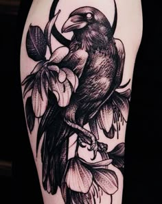 a black bird sitting on top of a tree branch with flowers around it's legs