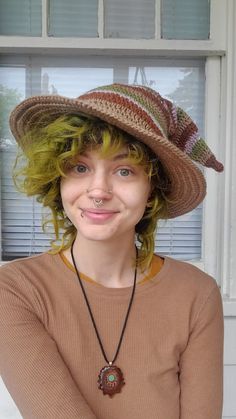 a woman with green hair wearing a brown sweater and hat, smiling at the camera