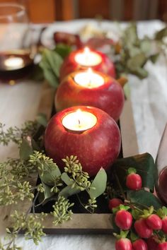 candles are lit in the shape of apples on a tray with greenery and berries