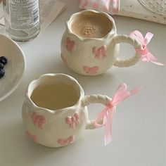 two coffee mugs with pink bows on them