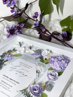 a wedding card with purple flowers and greenery in the middle, on a lace tablecloth