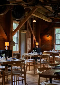 the interior of a restaurant with wooden tables and chairs in front of two large windows