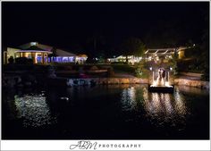 a bride and groom standing on a dock in front of their wedding venue at night