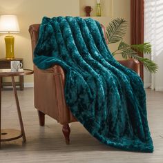 a couch covered in a teal blanket next to a table with a lamp on it