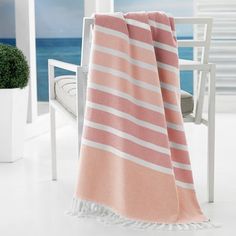 a pink and white striped towel sitting on top of a chair next to the ocean